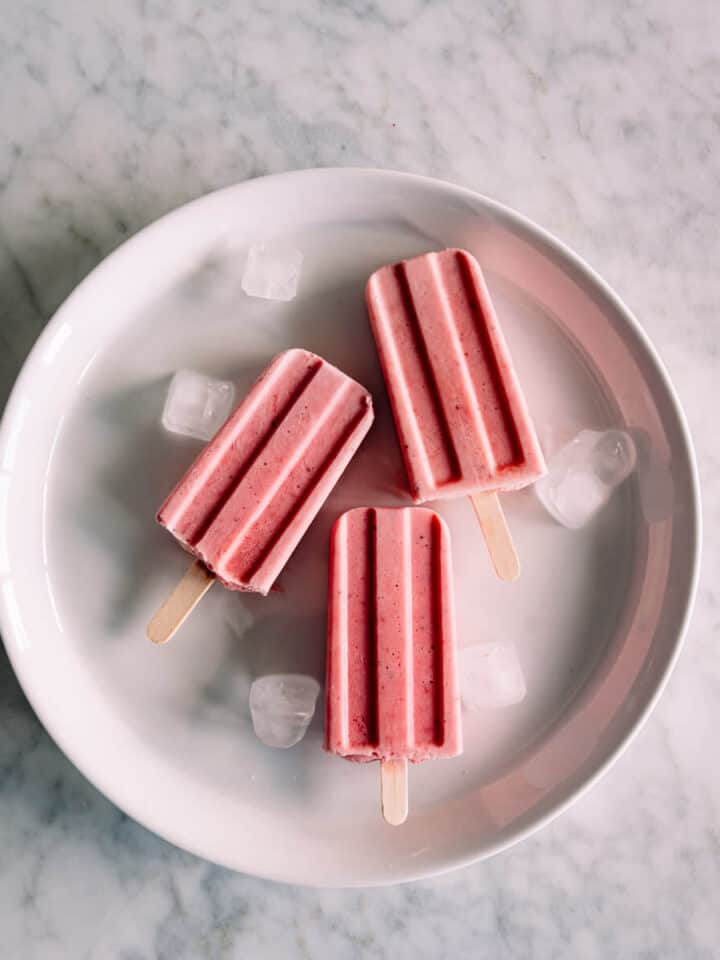 3 strawberry popsicles on a white plate.