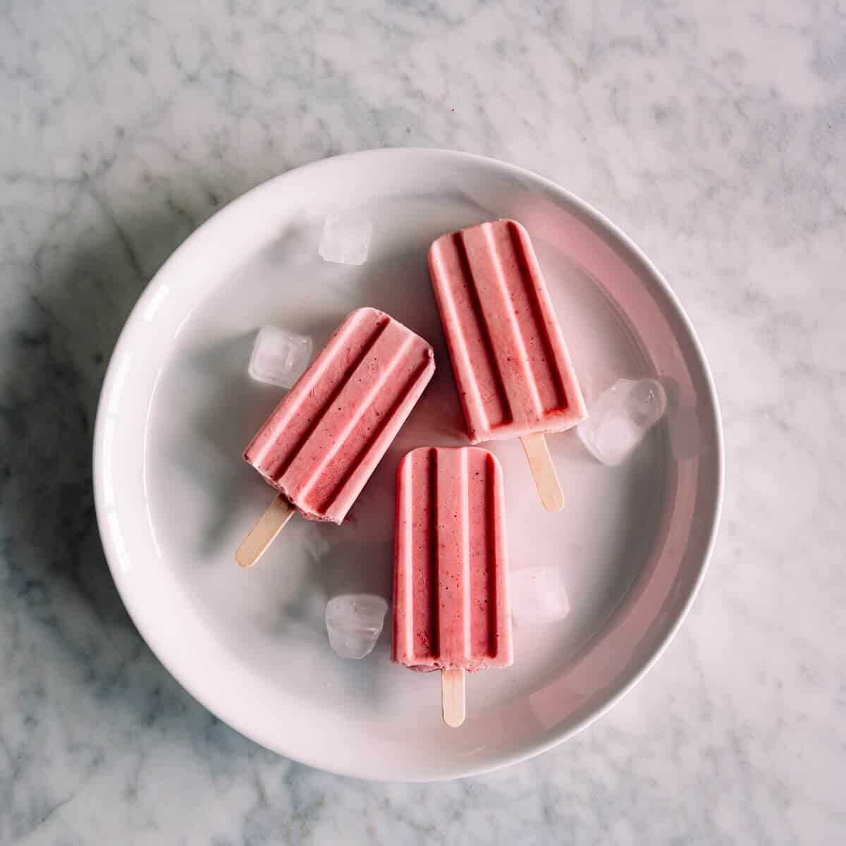 3 strawberry popsicles on a white plate.