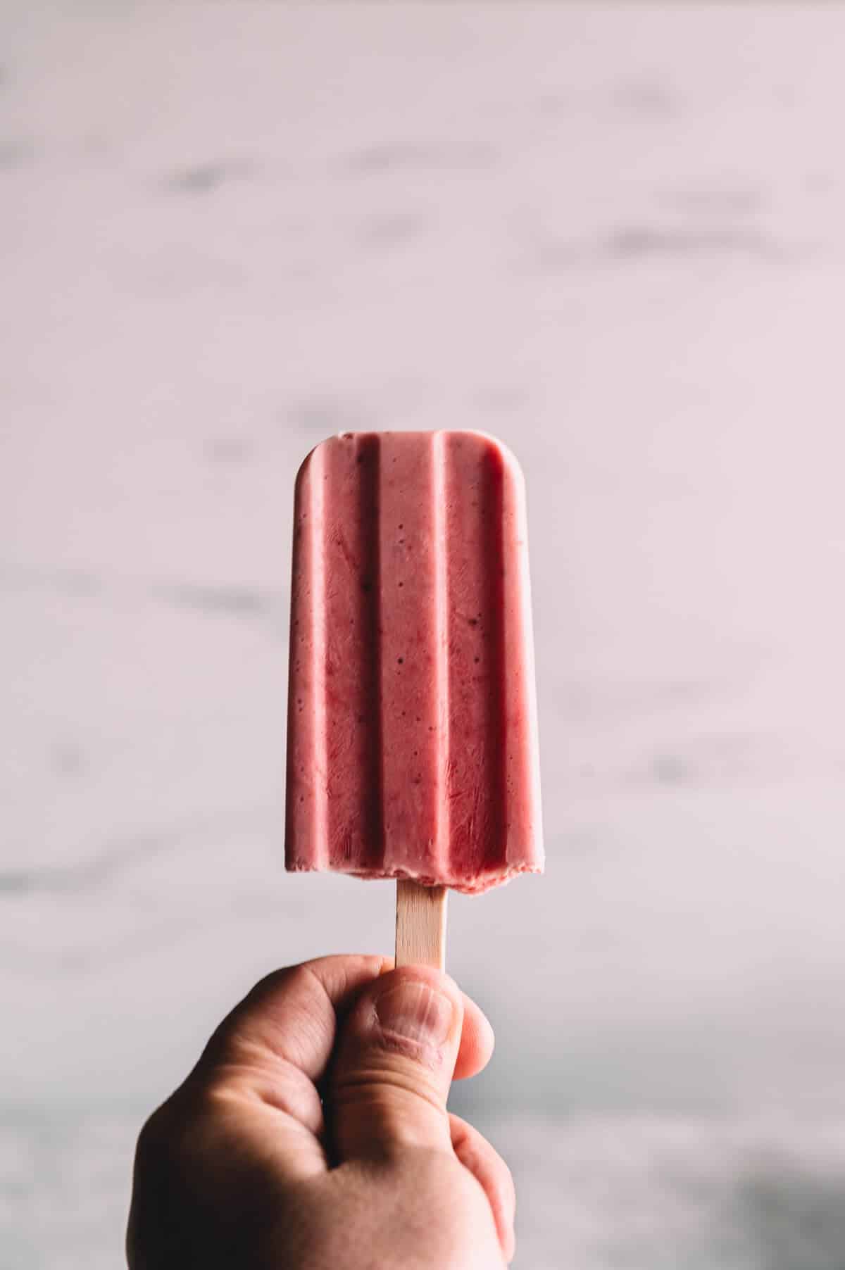 a hand holding a strawberry popsicle.