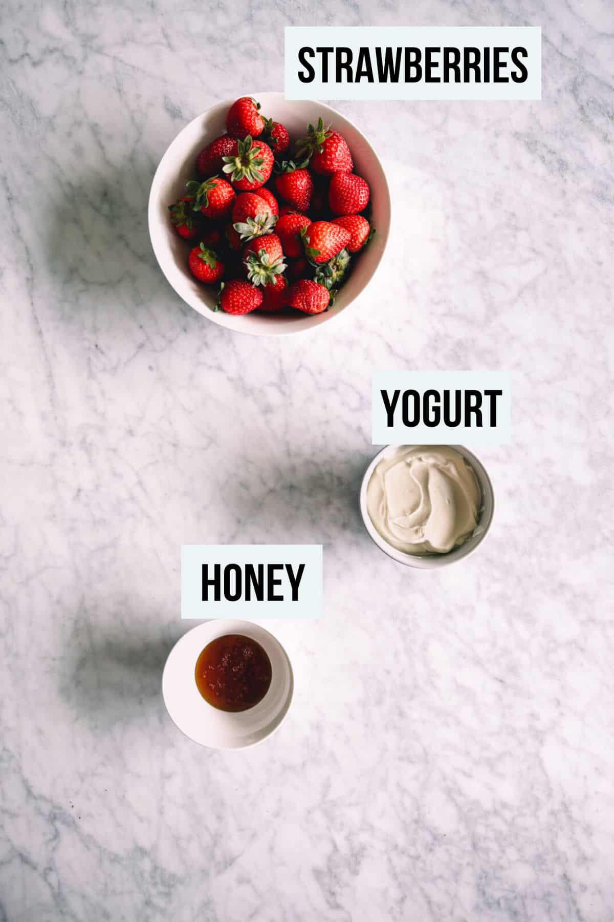 the ingredients to make strawberry popsicles on a white marble table.
