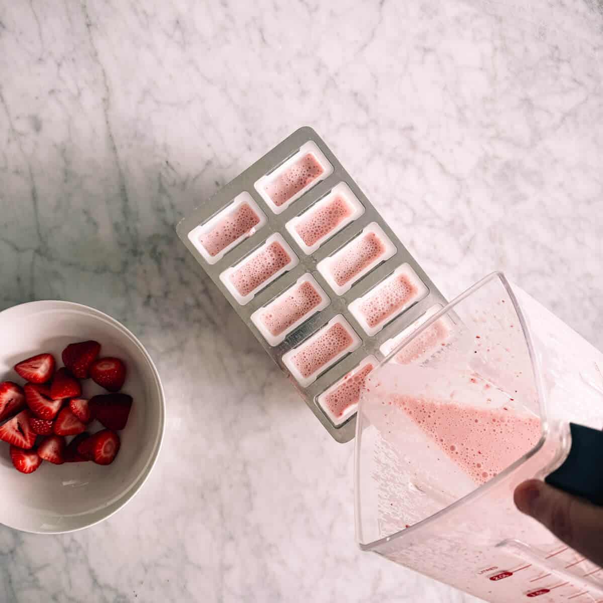 pouring liquid from a blender into a popsicle mold.