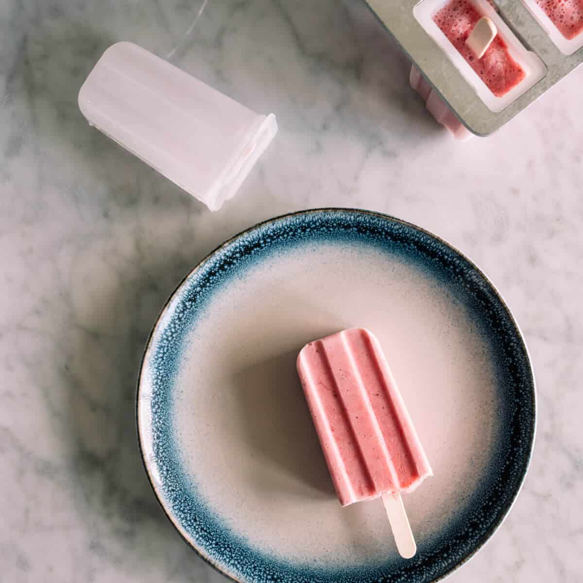a strawberry popsicle on a white plate with a blue rim.