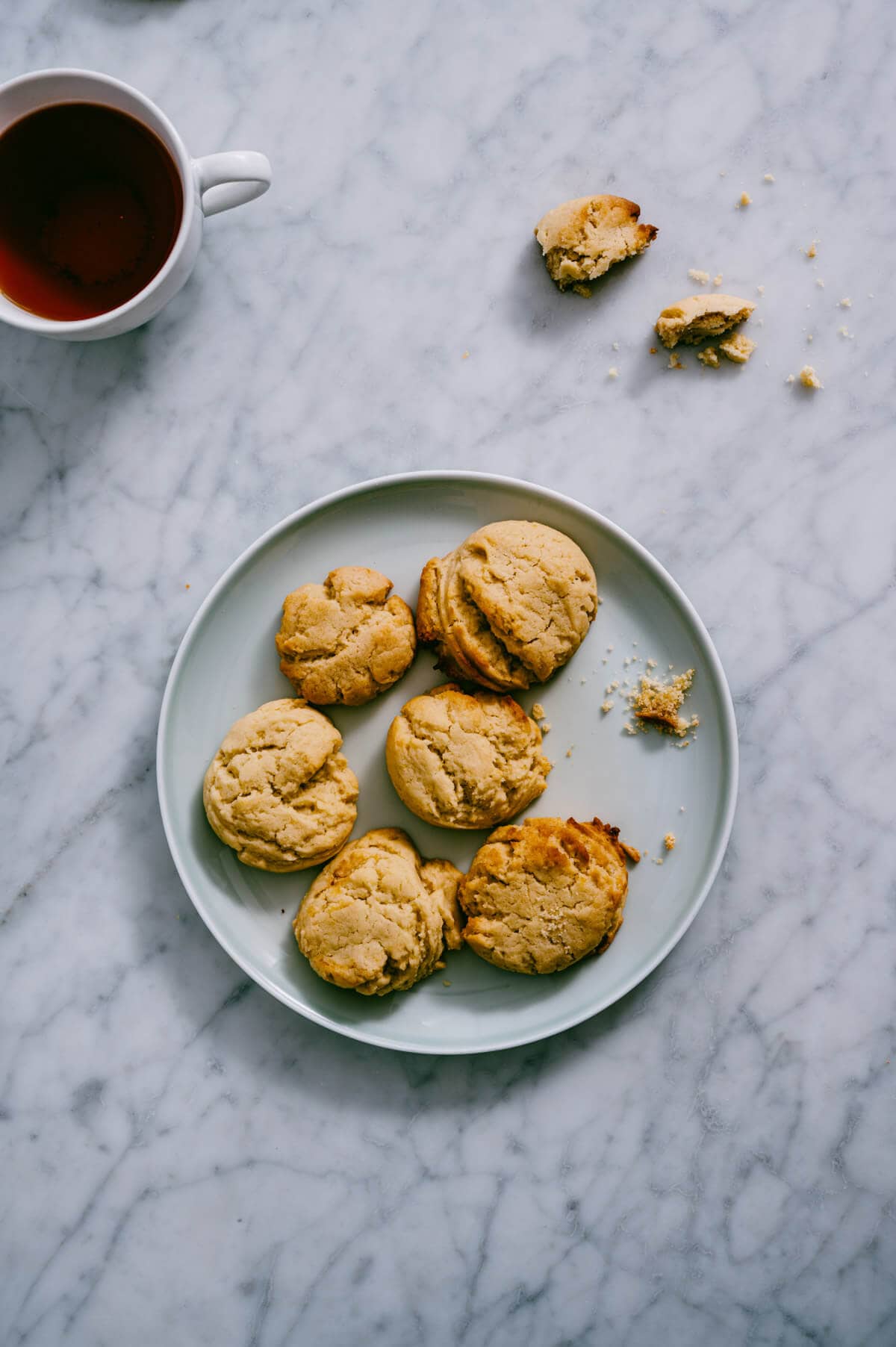 vegan lemon cookies presented on a plate with a cup of tea beside it.
