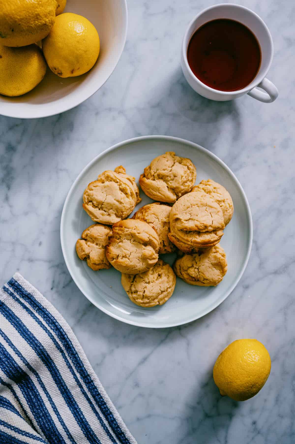 vegan lemon cookies on a plate with tea nd lemons surrounding it.