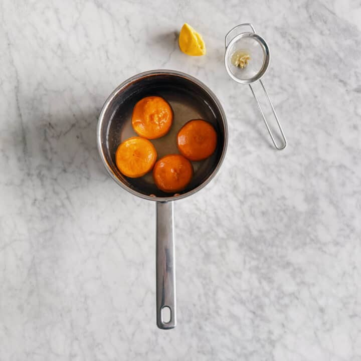 4 mandarins in a pot with water and half a sliced lemon on the side.