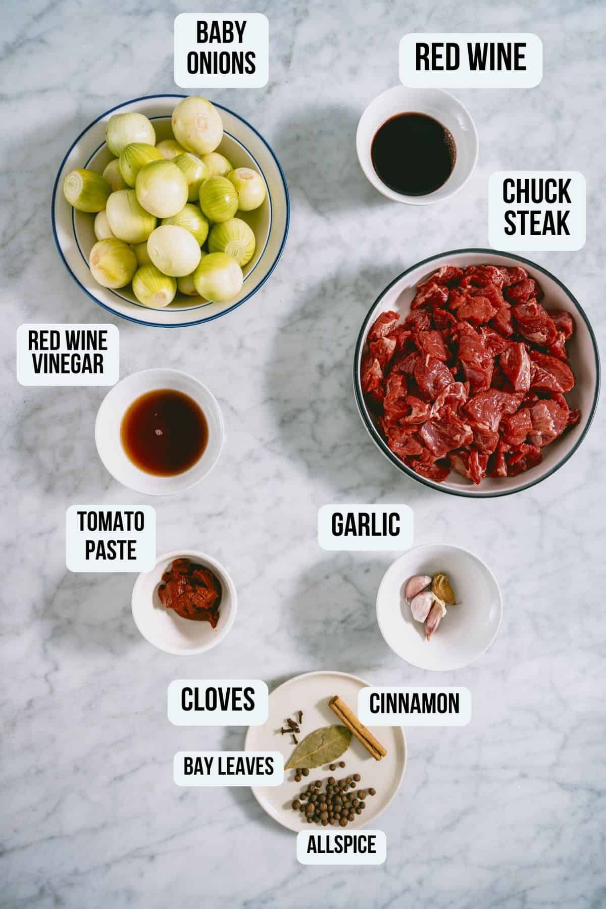 the ingredients to make beef stifado on a white marble table.