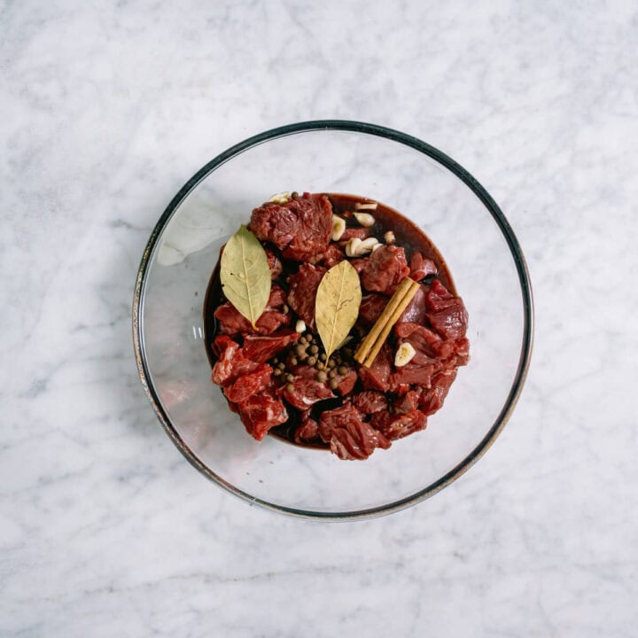 chuck steak and spices marinating in a glass bowl.