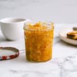 a jar of mandarin jam on a white marble table.