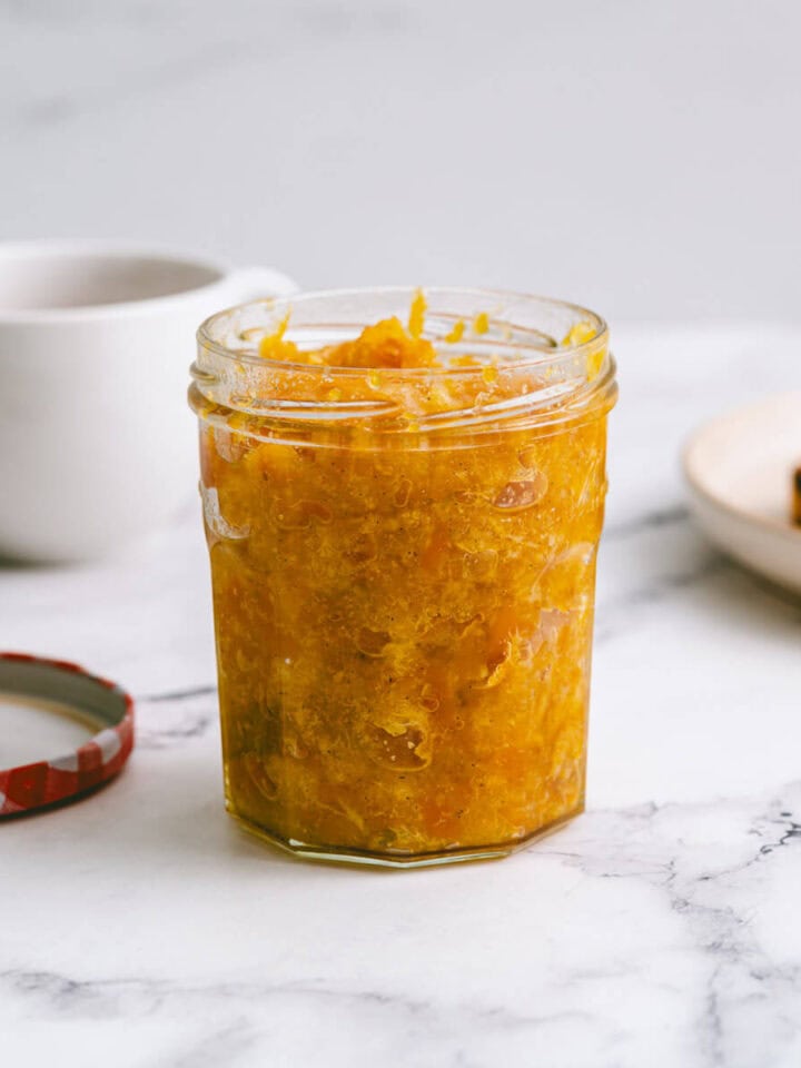 a jar of mandarin jam on a white marble table.