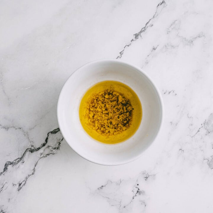 White bowl with garlic and olive oil dressing for tomato and halloumi salad on a marble background.