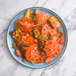 Blue plate with tomato and halloumi salad, topped with croutons and fresh basil.