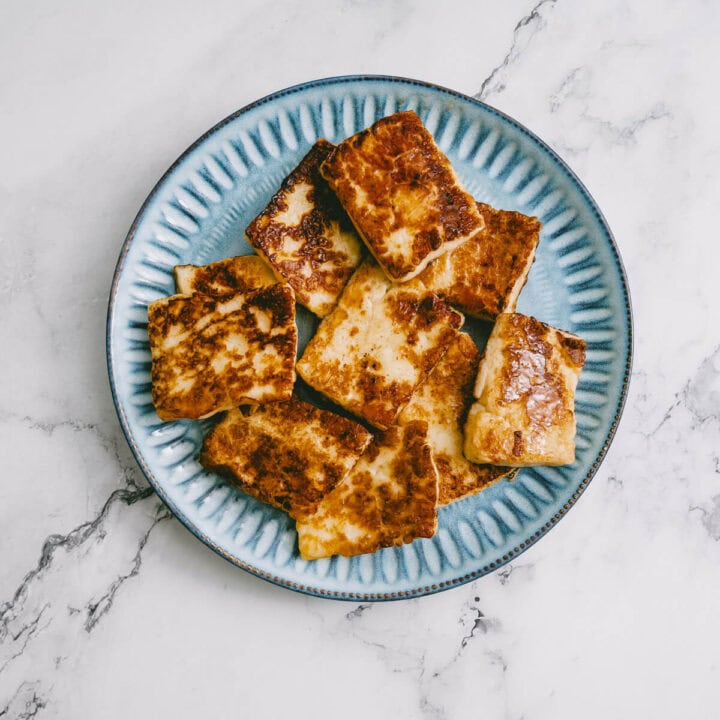 Golden brown halloumi slices on a blue plate, ready to be used in salad.