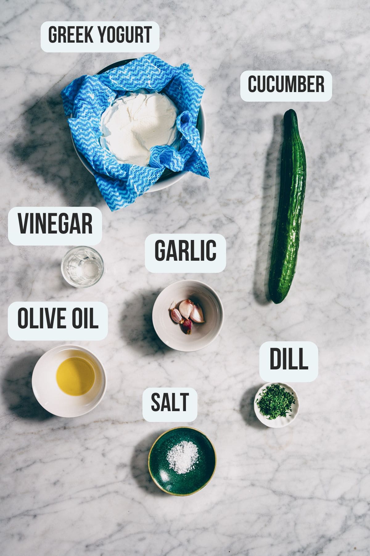 Ingredients for Greek tzatziki laid out on a marble surface.