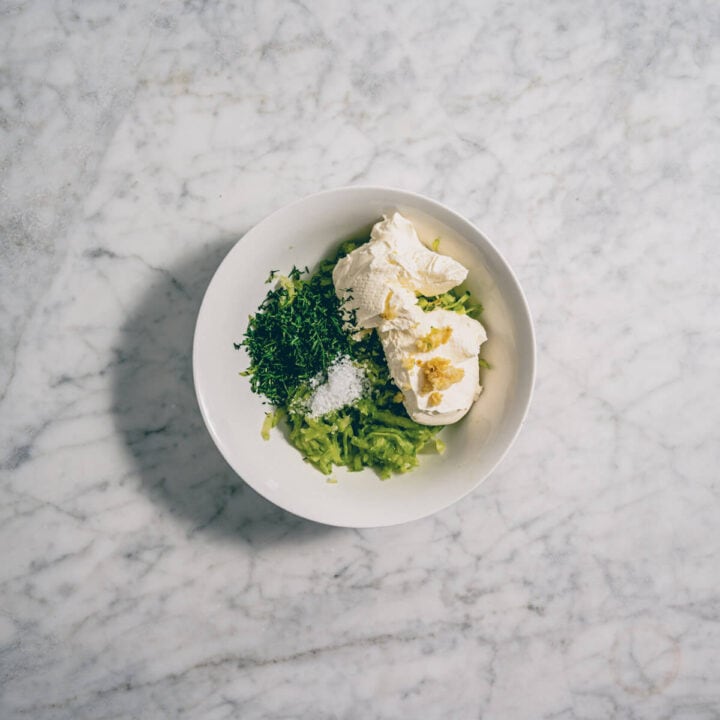 Bowl with yogurt, cucumber, garlic, dill, and salt ready to be mixed into tzatziki.