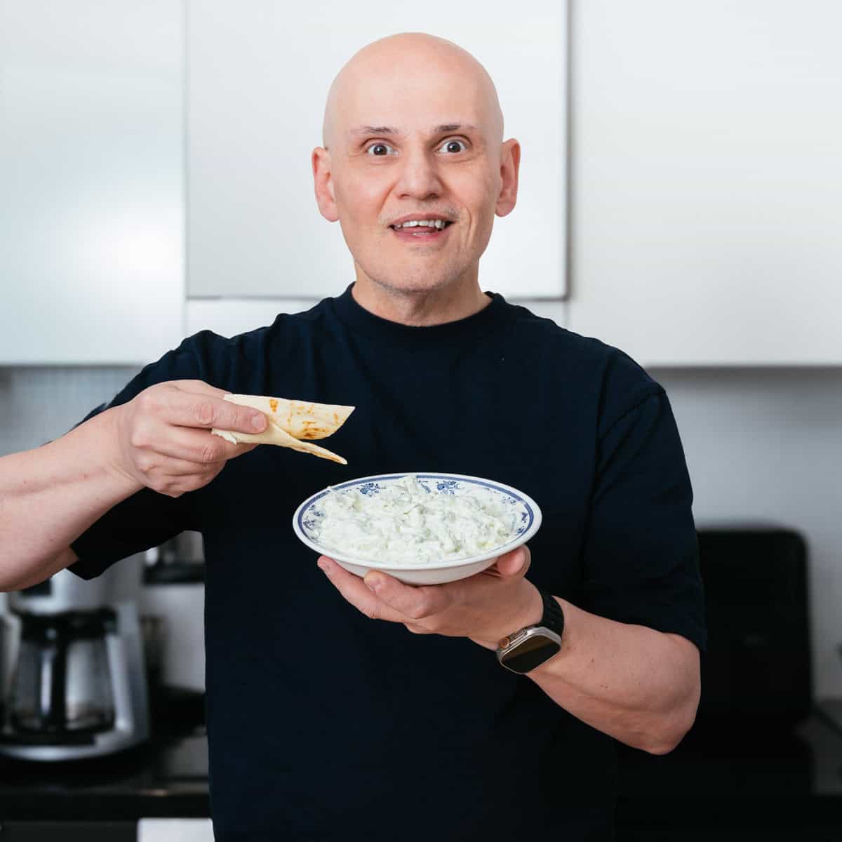 Peter holding a bowl of homemade Greek tzatziki with pita bread.