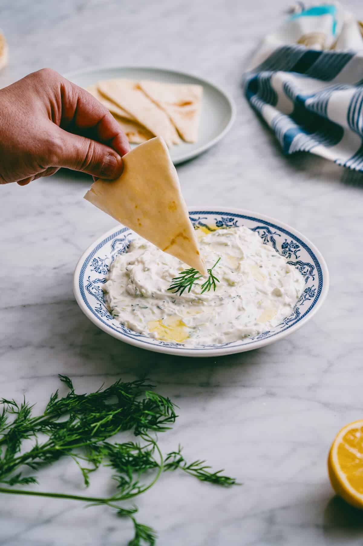 Hand dipping pita bread into a bowl of tzatziki.