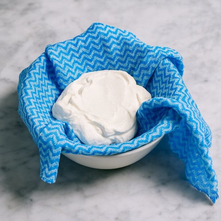 Greek yogurt straining in a blue cloth over a bowl to make thick tzatziki.
