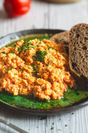 Close-up of creamy Greek style scrambled eggs with tomatoes on a green plate, served with slices of dark bread.