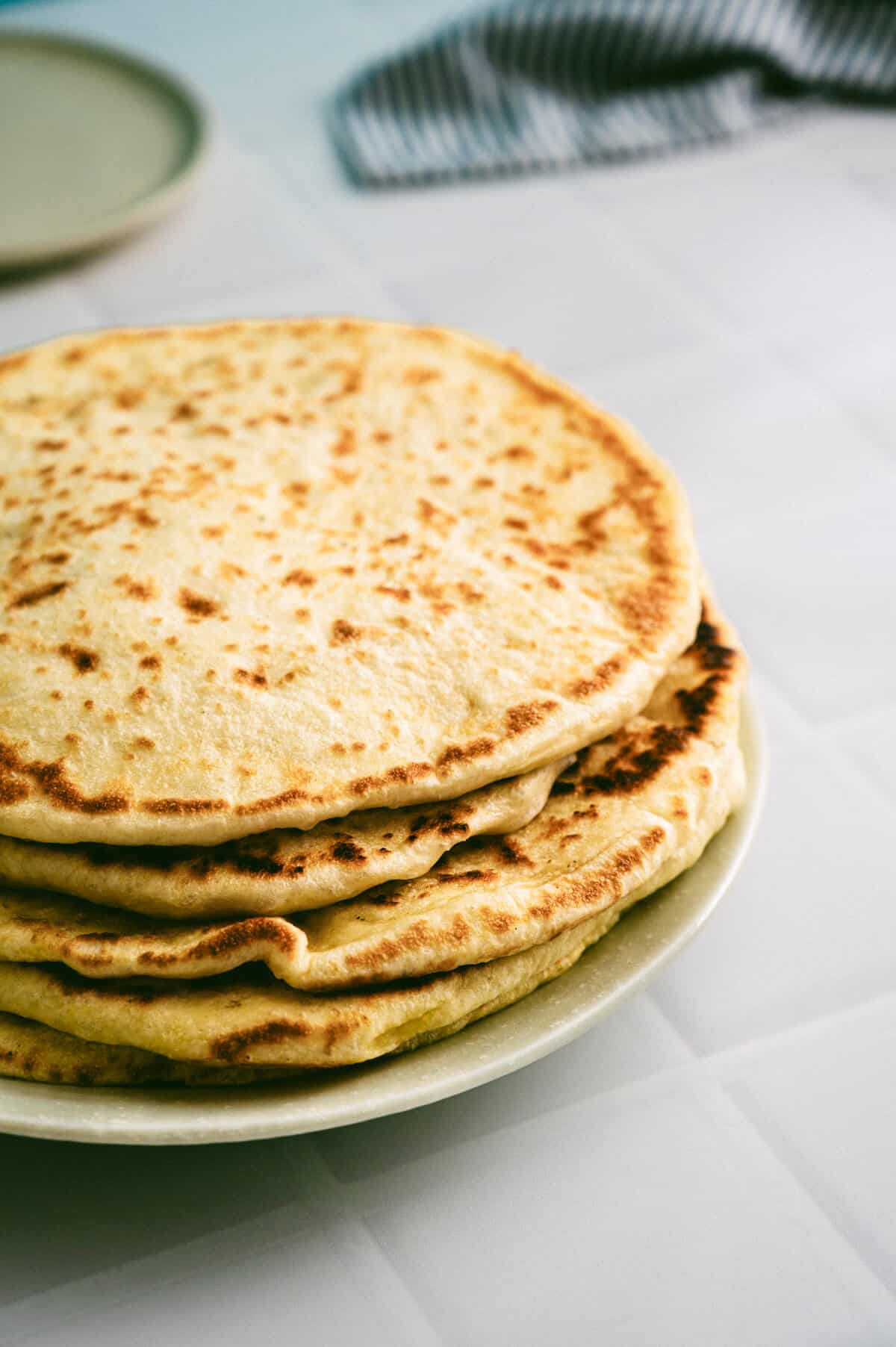 Soft Greek pita bread stacked on a plate, lightly golden with charred spots.
