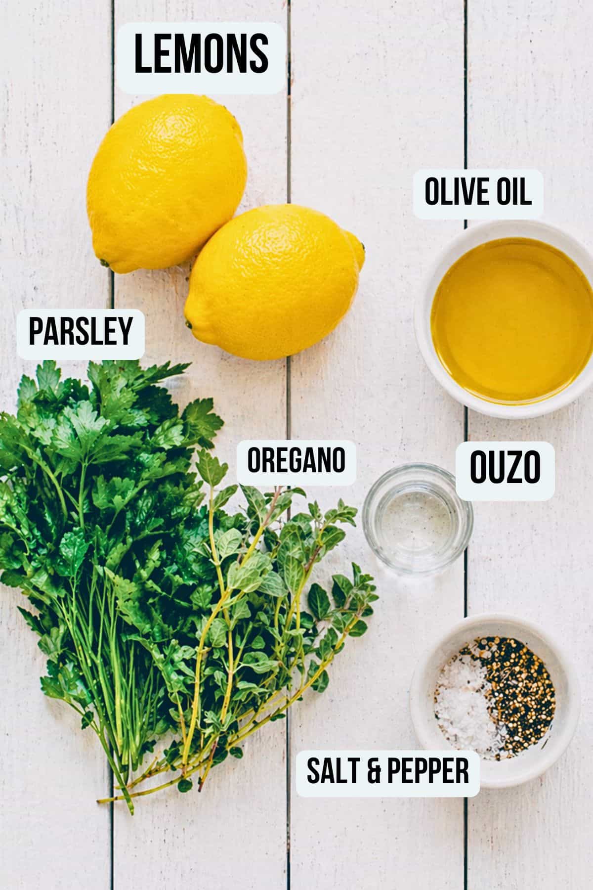 Ingredients for Greek salad dressing including lemons, olive oil, parsley, oregano and ouzo on a white surface.