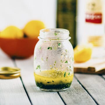 Greek salad dressing made with olive oil, lemon juice and herbs in a small glass jar.