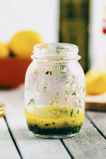 Greek salad dressing made with olive oil, lemon juice and herbs in a small glass jar.