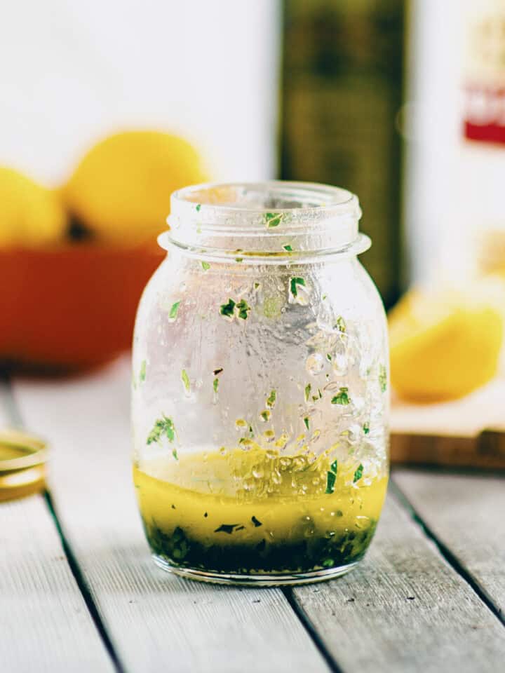 Greek salad dressing made with olive oil, lemon juice and herbs in a small glass jar.