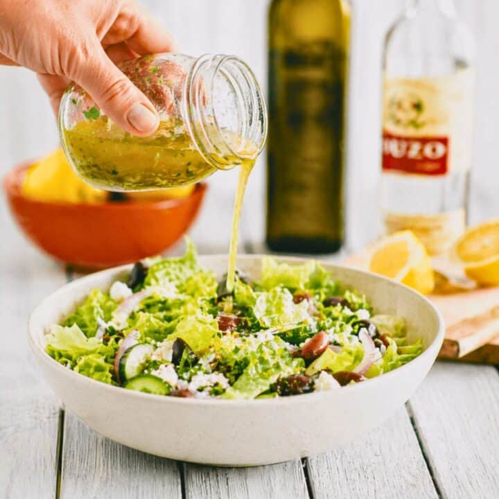 Greek salad dressing with ouzo being poured over a fresh salad with olives, cucumber and feta.