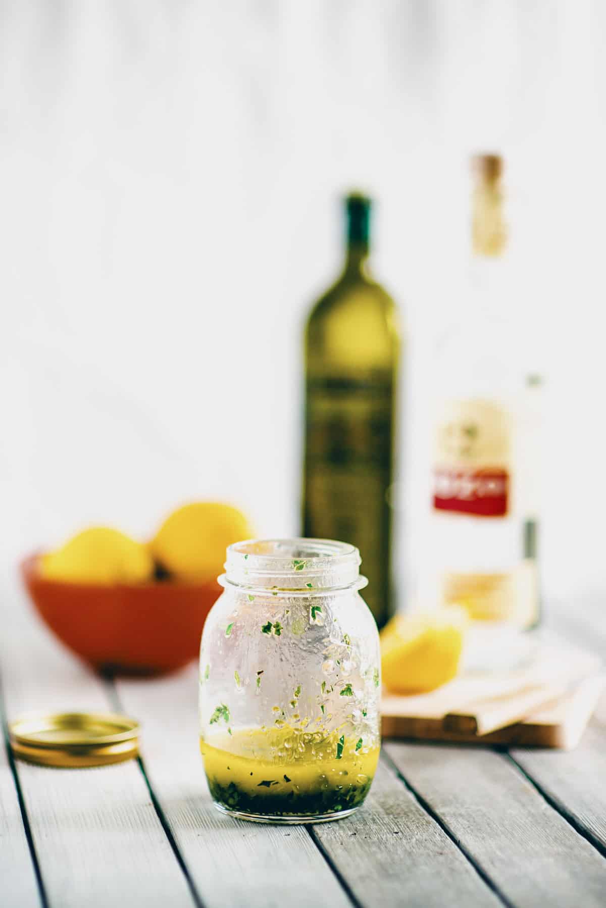 Greek salad dressing with ouzo in a glass jar on a wooden table with a soft blurred background.