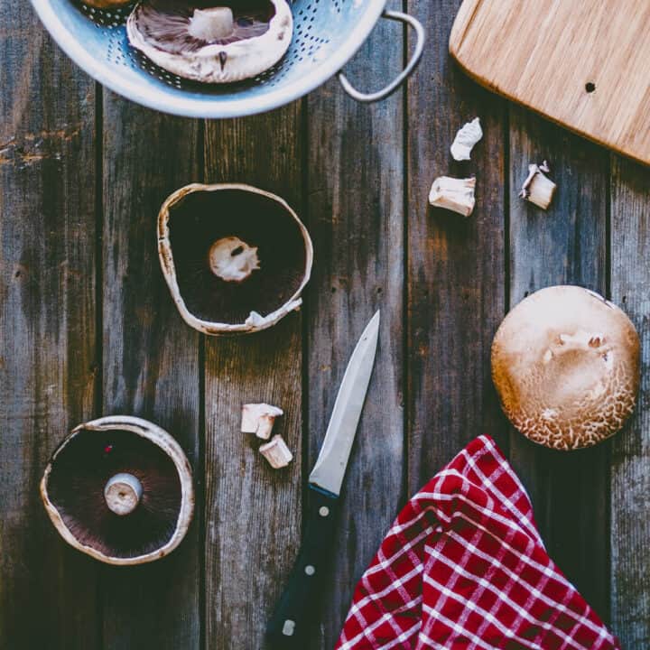 Preparing portobello mushrooms for stuffing with stems removed on wooden surface with knife and kitchen towel.
