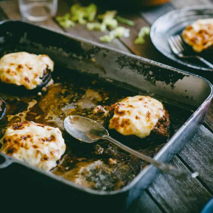 Ground beef stuffed mushrooms baking in oven tray topped with creamy sauce and cheese.