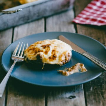 Ground beef stuffed portobello mushroom topped with melted cheese served on a blue plate.