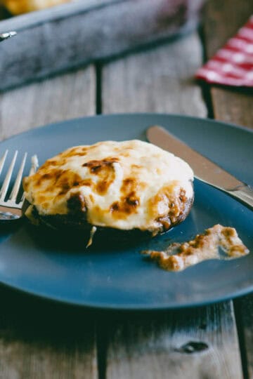 Ground beef stuffed portobello mushroom topped with melted cheese served on a blue plate.