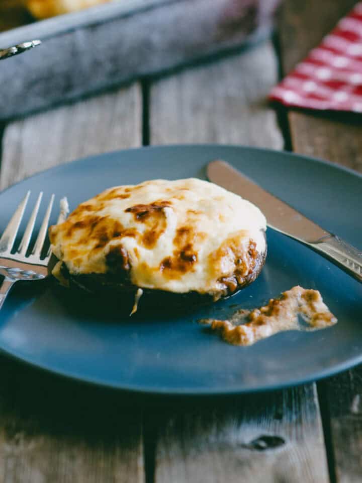 Ground beef stuffed portobello mushroom topped with melted cheese served on a blue plate.