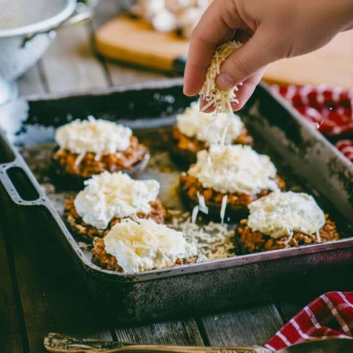 Adding grated cheese to ground beef stuffed mushrooms before baking in oven tray.