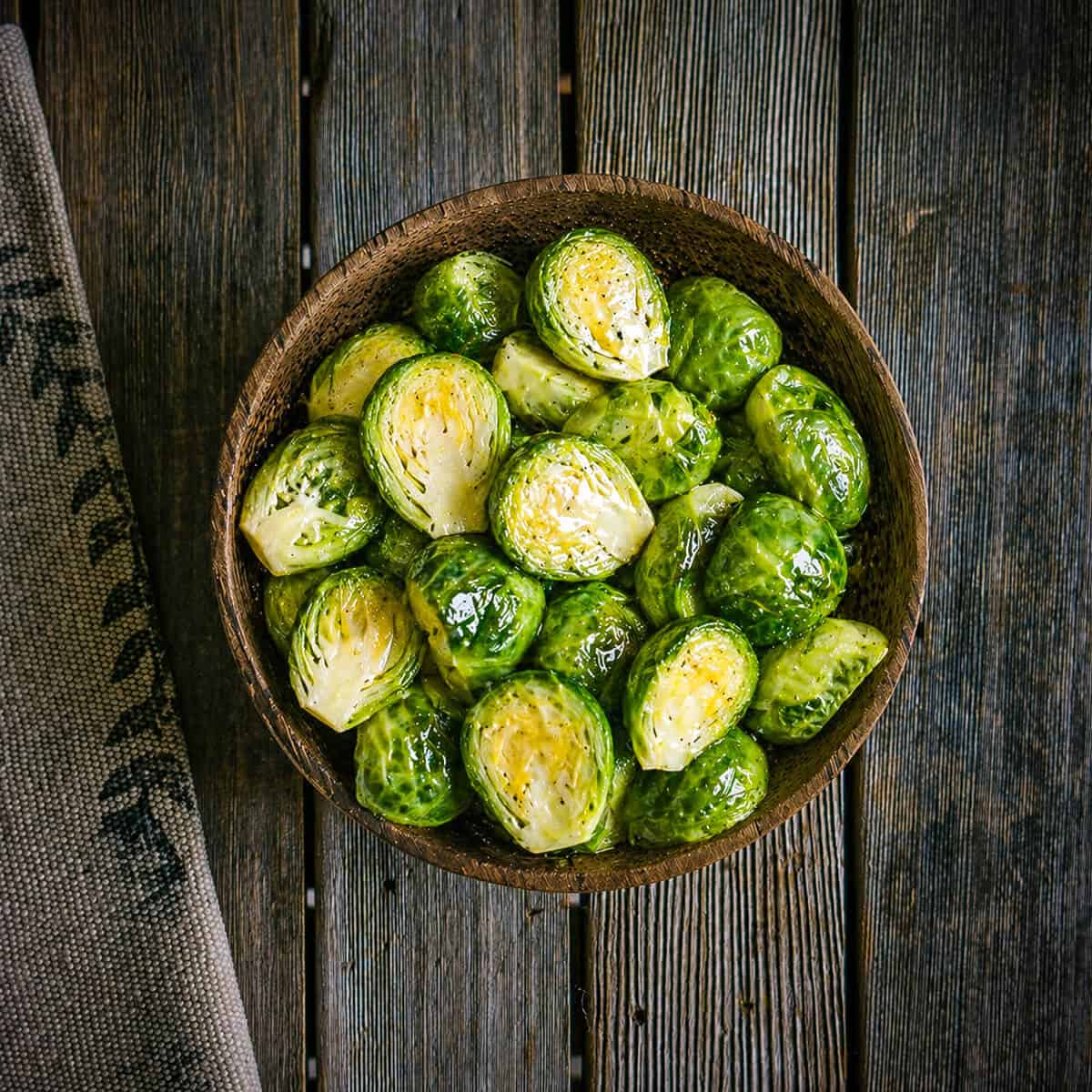 Halved Brussels sprouts tossed with olive oil in a wooden bowl.