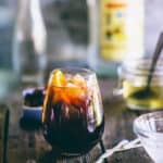 Greek ouzo cocktail with coffee liqueur and orange served over ice in a rounded glass.