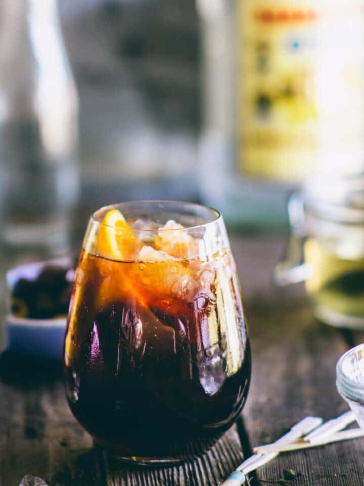 Greek ouzo cocktail with coffee liqueur and orange served over ice in a rounded glass.