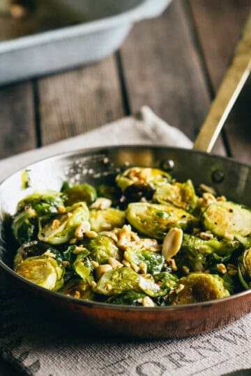 Pan of roasted Brussels sprouts with honey and peanuts on a rustic wooden table.