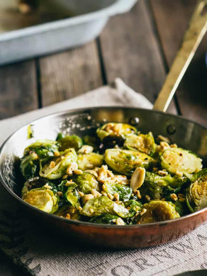 Pan of roasted Brussels sprouts with honey and peanuts on a rustic wooden table.
