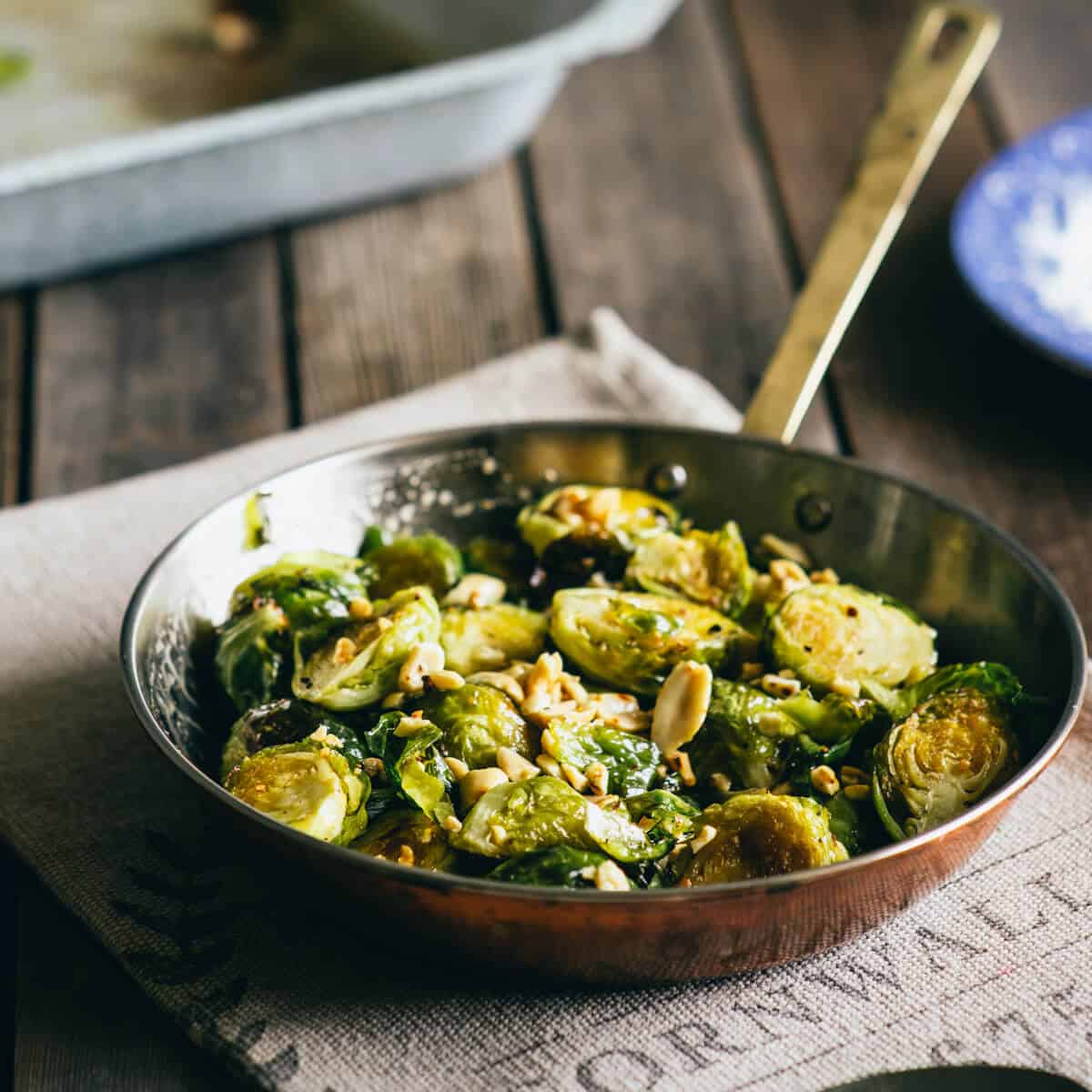 Pan of roasted Brussels sprouts with honey and peanuts on a rustic wooden table.