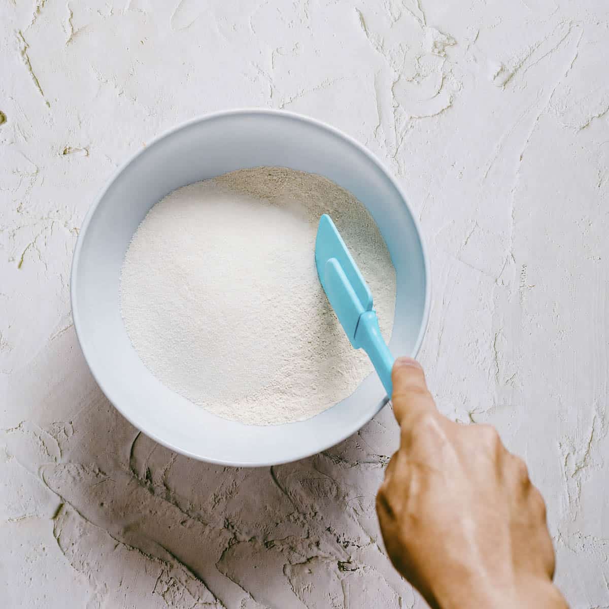 dry ingredients being mixed in a light blue bowl to make baked cake doughnuts.