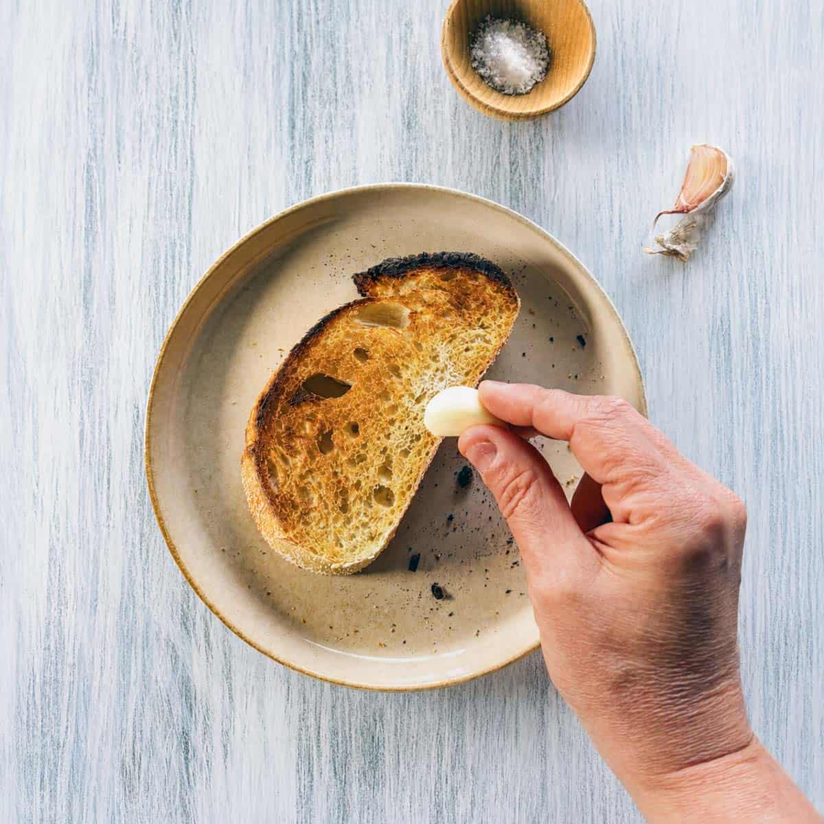 toasted sourdough being rubbed with a garlic bulb.