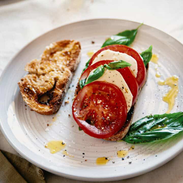 caprese bruschetta served on a plate with an extra slice of toasted bread.