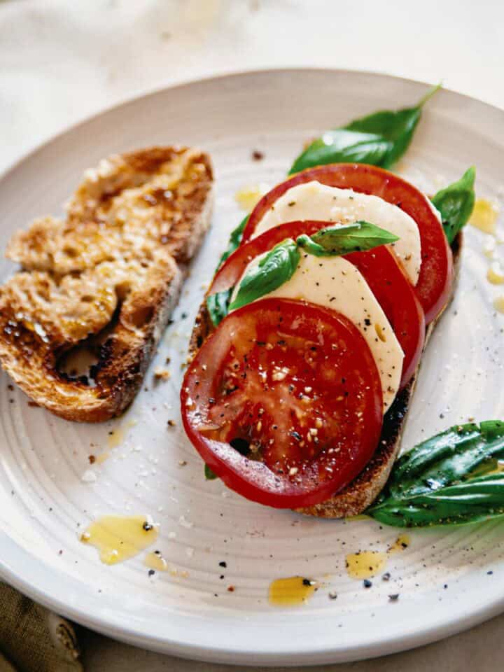 caprese bruschetta served on a plate with an extra slice of toasted bread.