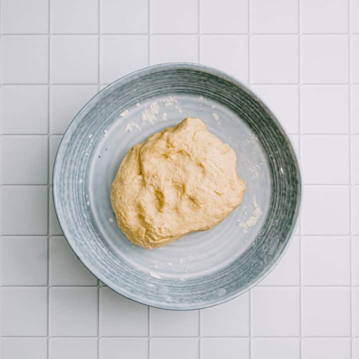 Dough for chickpea flatbread resting on a plate with flour.