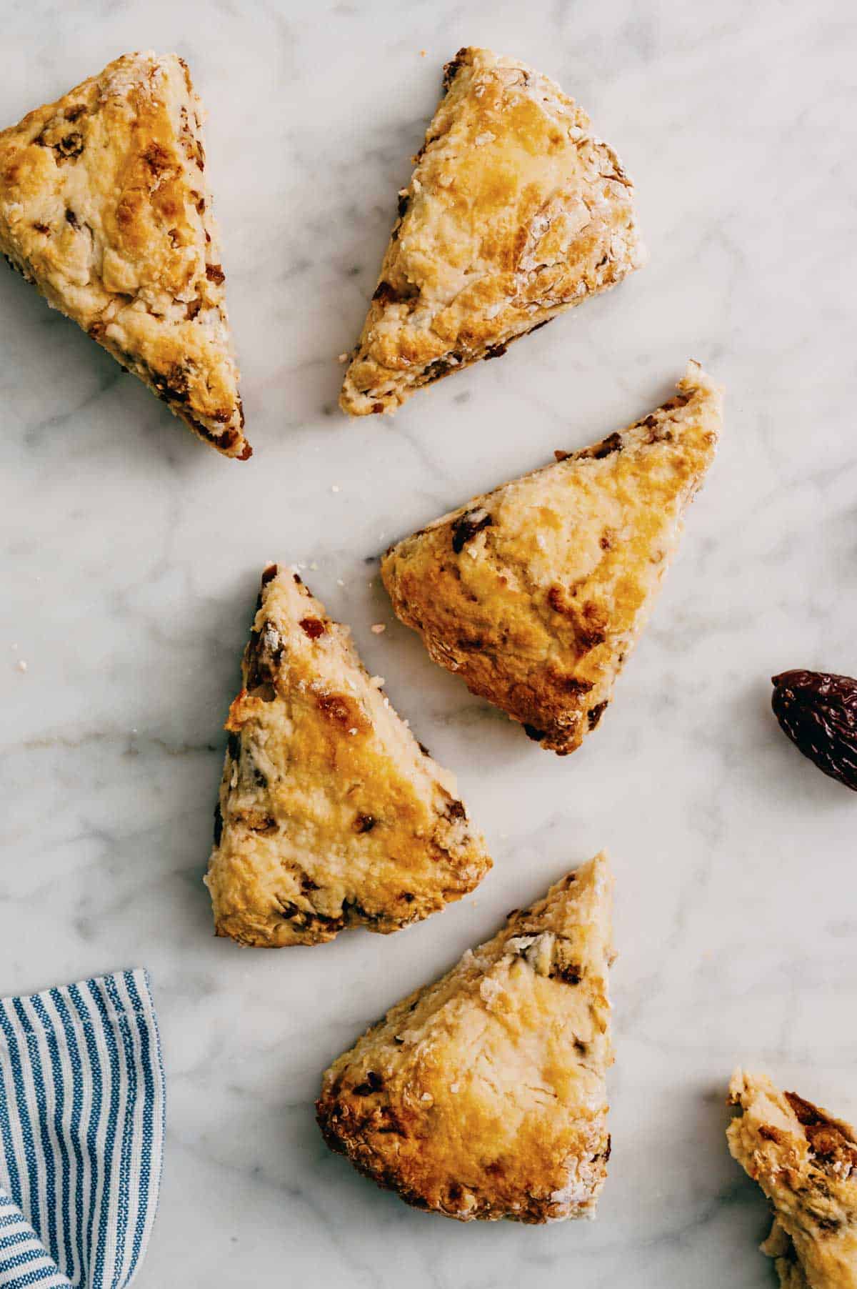 baked date scones arranged on marble with cloth and scattered crumbs.