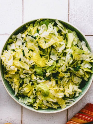 a bowl of Greek lettuce salad served on a tiled table.