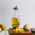 Glass bottle of lemon infused olive oil on a wooden board with peeled lemons.