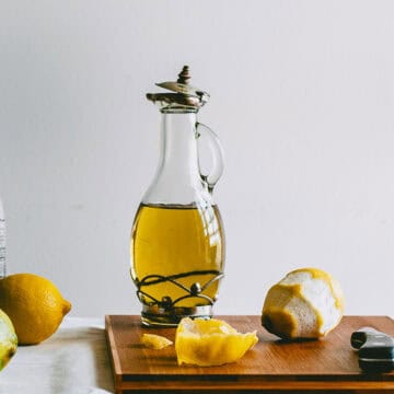 Glass bottle of lemon infused olive oil on a wooden board with peeled lemons.